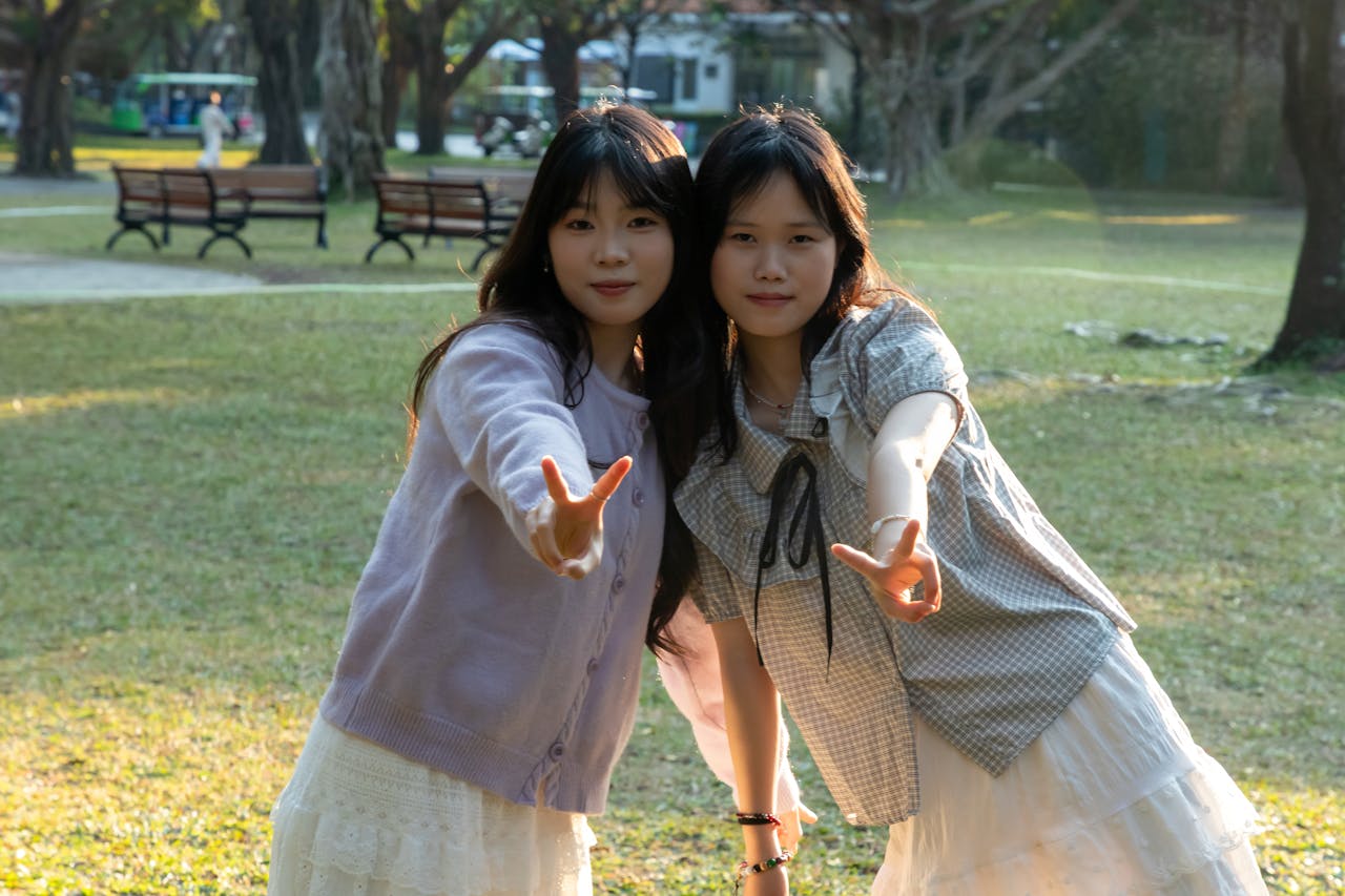 Two young women posing with peace signs in a sunny park setting.